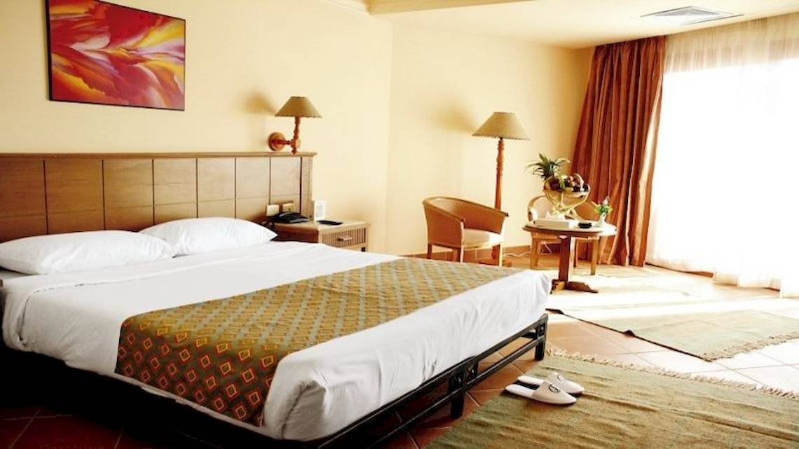 Ein elegantes Hotelzimmer im Charmillion Garden Aqua Park mit Doppelbett, Nachttischen, Stühlen und Gemälde an der Wand.