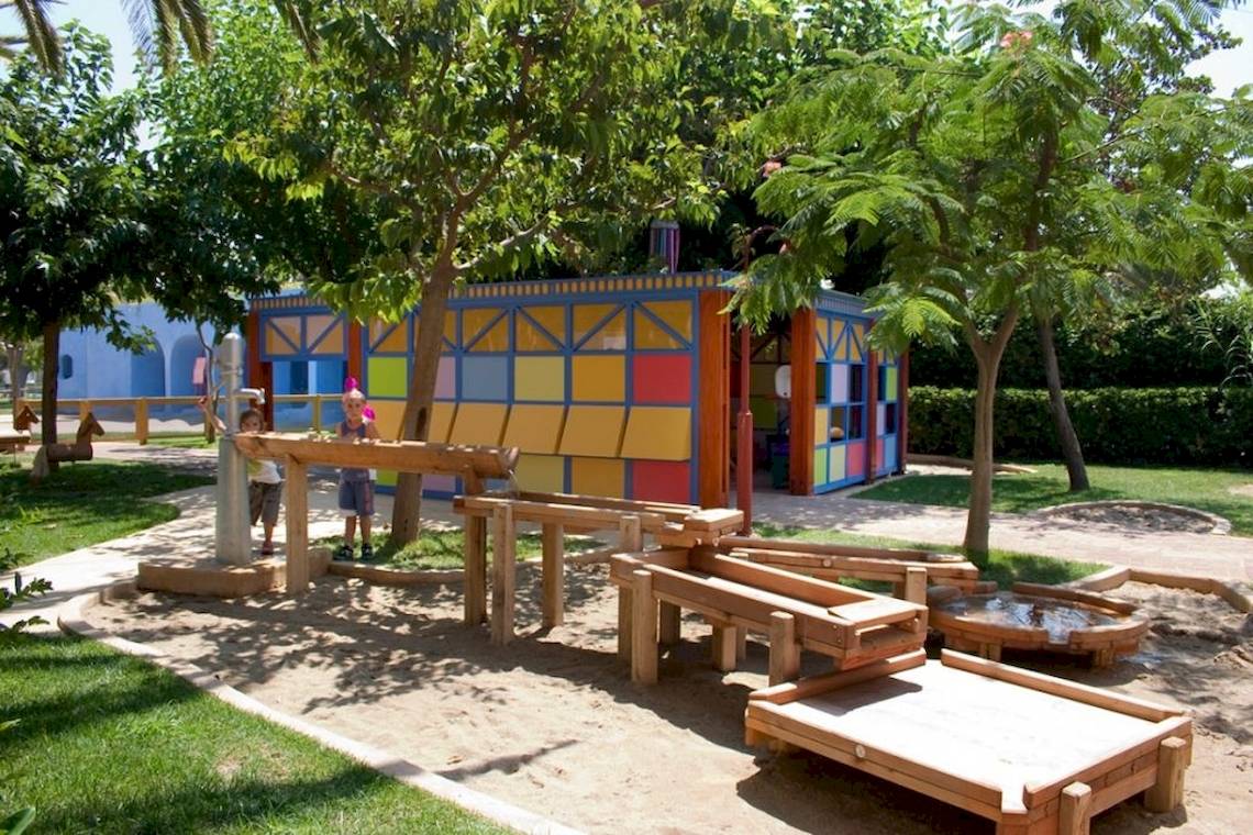 Kinderspielplatz im Freien mit bunten Gebäuden und Holzspielzeug im Sand.