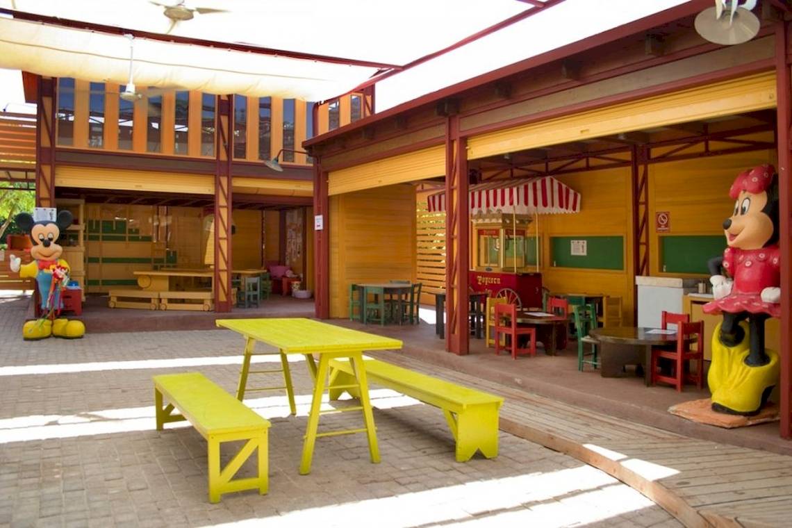 Außenbereich des Aquila Rithymna Beach Hotels mit gelben Tischen und Bänken und Mickey Mouse Statue.