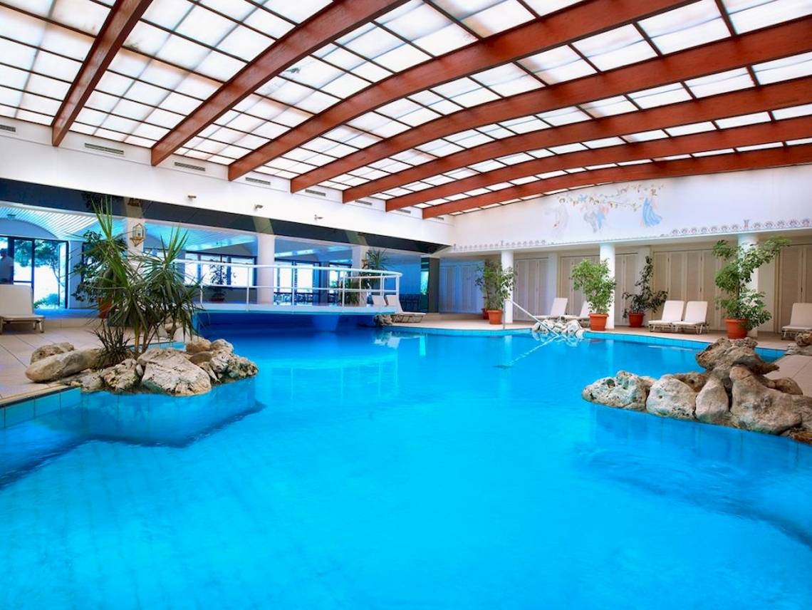Innenpool im Aquila Rithymna Beach Hotel mit blauem Wasser und steinernen Dekorationen.