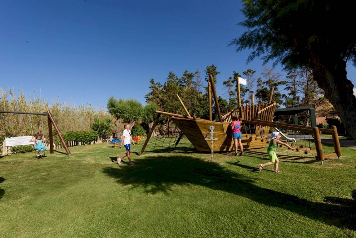 Kinder spielen auf einem Spielplatz im Freien, der ein Piratenschiff und eine Schaukel hat.