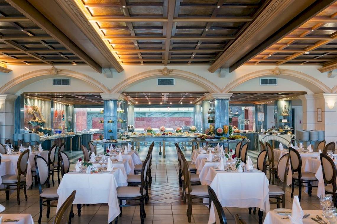 Innenansicht des Restaurants im Aquila Rithymna Beach Hotel mit gedeckten Tischen und Stühlen.