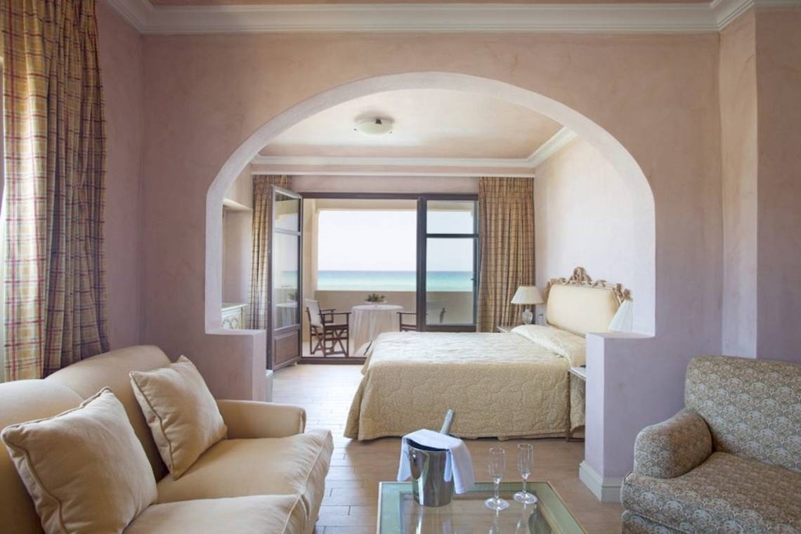 Aquila Rithymna Beach Hotel Zimmer mit Meerblick, Bett, Sofa und Tisch mit Champagnergläsern.