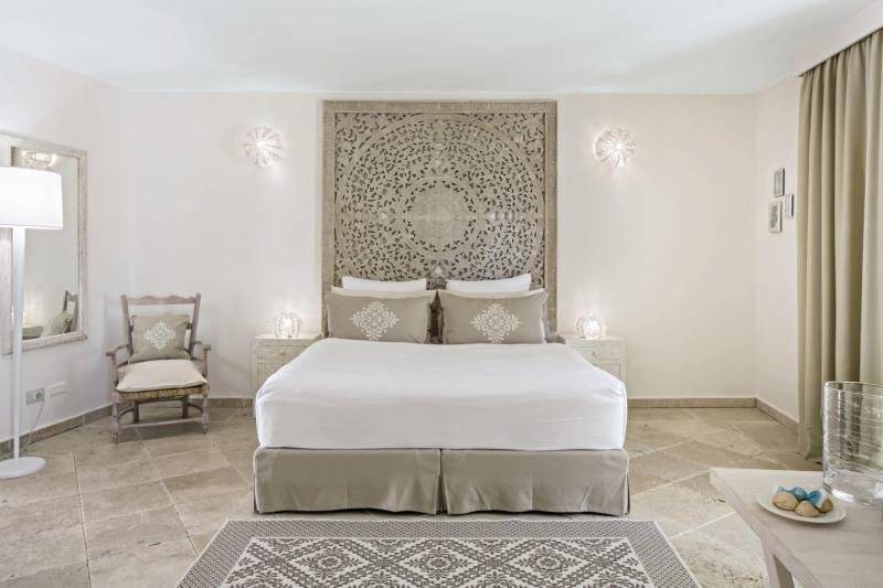 Innenansicht eines Schlafzimmers im Falkensteiner Resort Capo Boi mit großem Bett und kunstvollen Wanddekorationen.