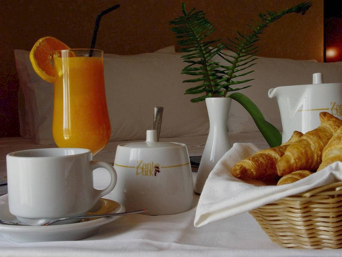 Frühstückstisch im Zante Park Resort & Spa mit Orangensaft, Croissants, Kaffeetasse und Pflanzen