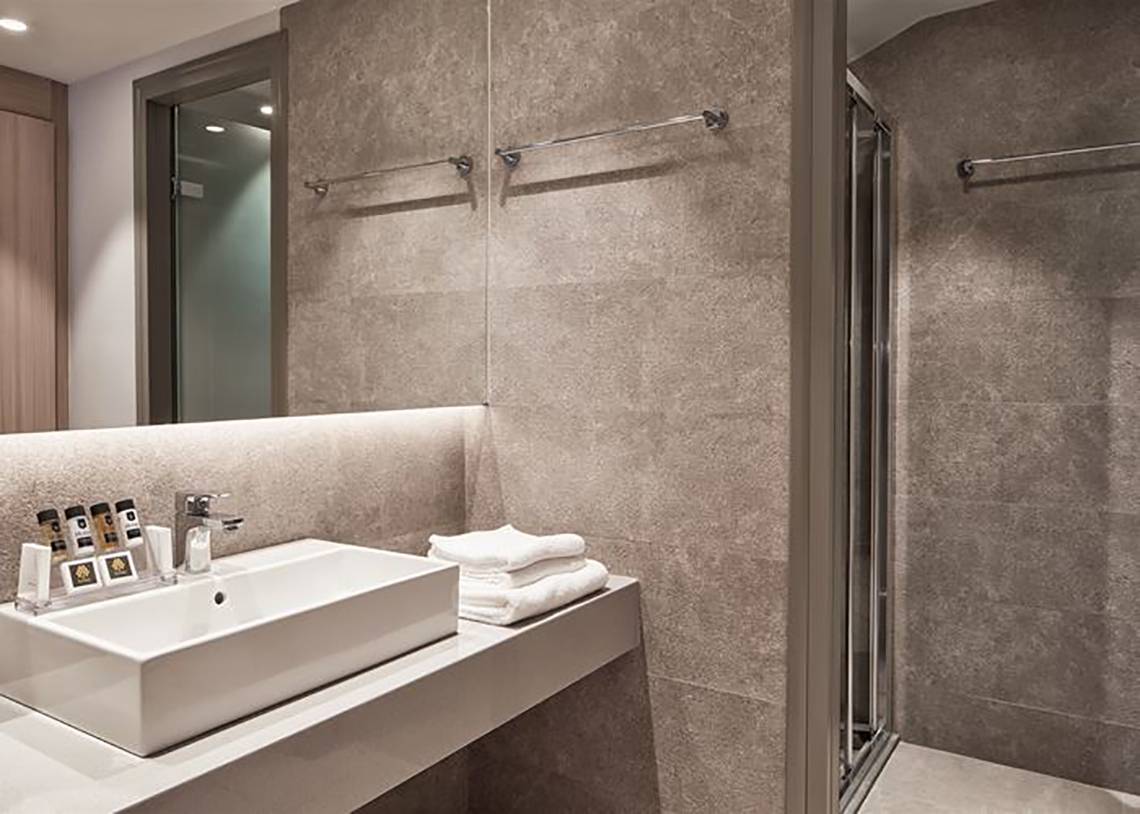 Badezimmer im Porto Bello Royal Hotel mit Waschbecken, Handtüchern und Duschbereich.