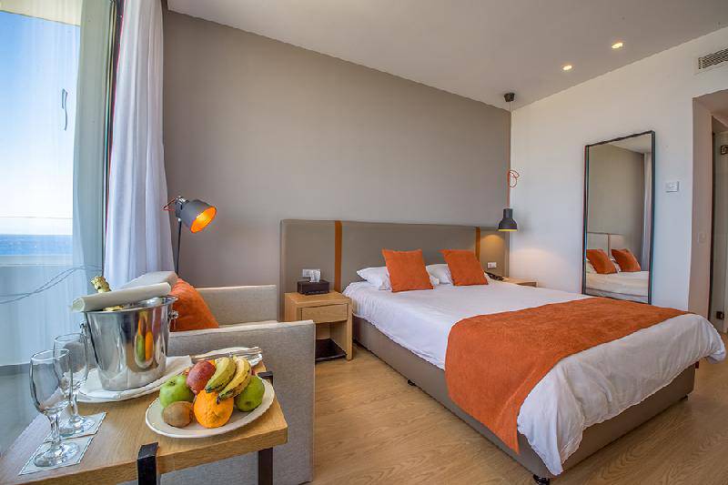 Innenansicht eines Zimmers im Crystal Springs Beach Hotel mit Meerblick, einem Bett, einem Schreibtisch und Obstteller.