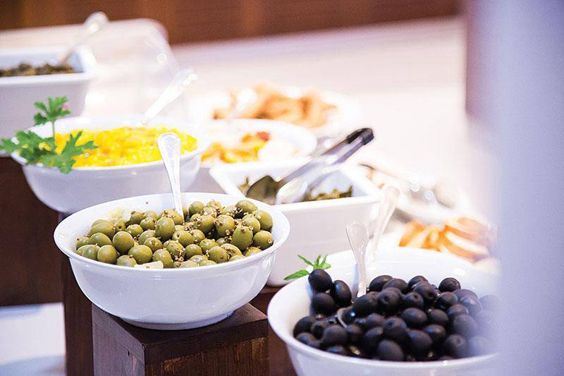 Buffet-Tisch mit verschiedenen Speisen, darunter grüne und schwarze Oliven, serviert in weißen Schüsseln.