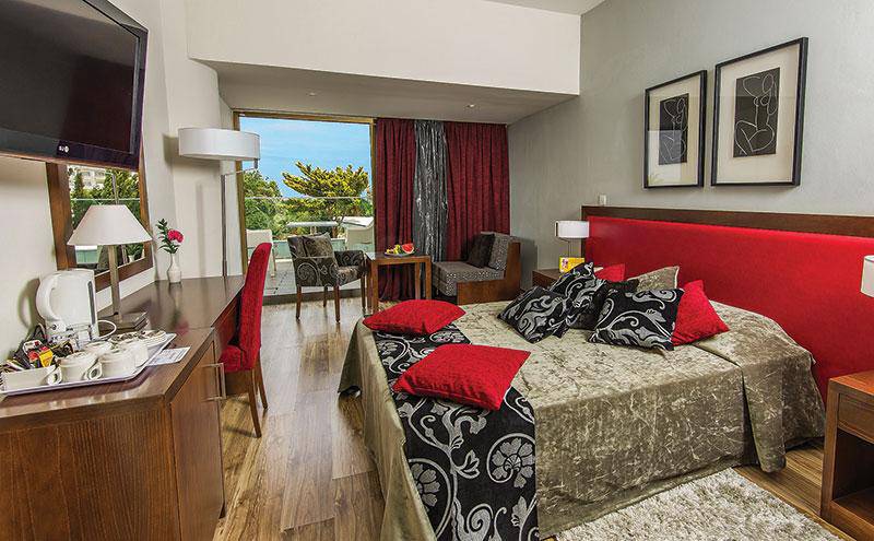Schlafzimmeransicht im Kristall Springs Beach Hotel mit einem großen Bett, rotem Kopfteil und Blick auf den Balkon.