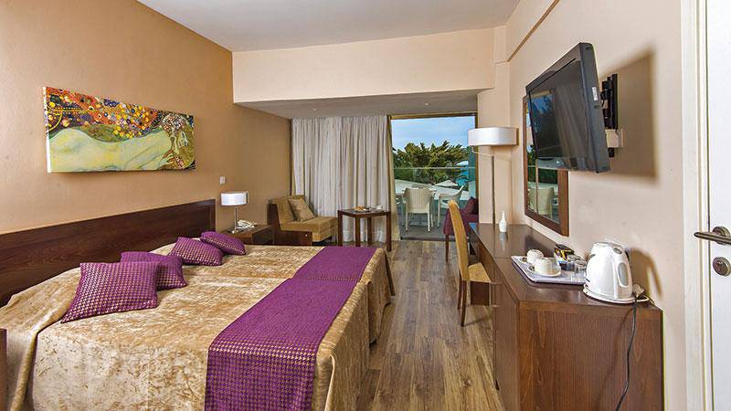 Innenansicht eines Zimmers im Crystal Springs Beach Hotel mit Bett, Fernseher und Balkon.