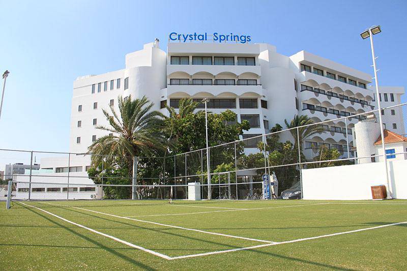 Außenansicht des Crystal Springs Beach Hotels mit Tennisplatz und Gebäude im Hintergrund.