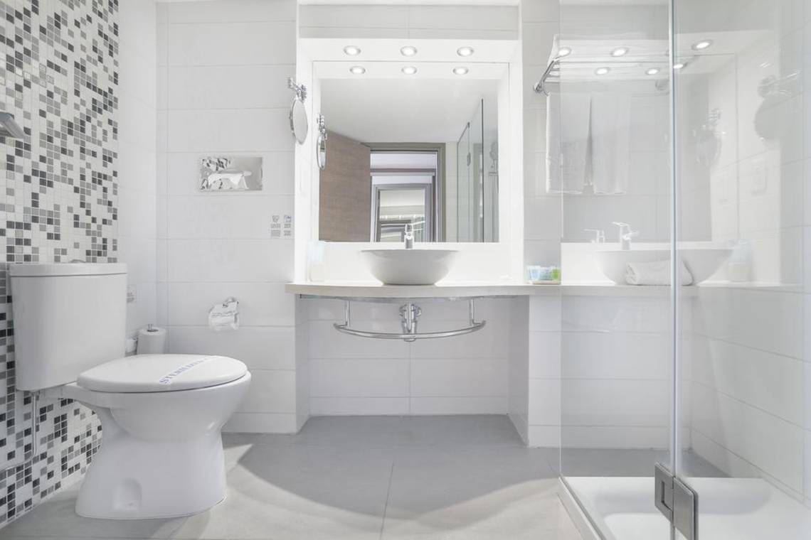 Modernes Badezimmer im Vassos Nissi Plage Hotel mit weißem Design und Glasdusche.