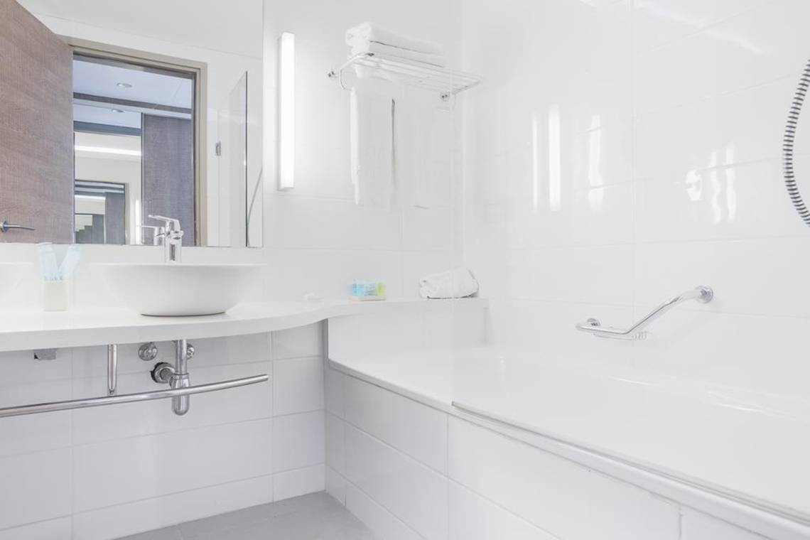 Ein weißes Badezimmer mit einer Badewanne, einem Waschbecken und einem Fenster im Hotel Vassos Nissi Plage.