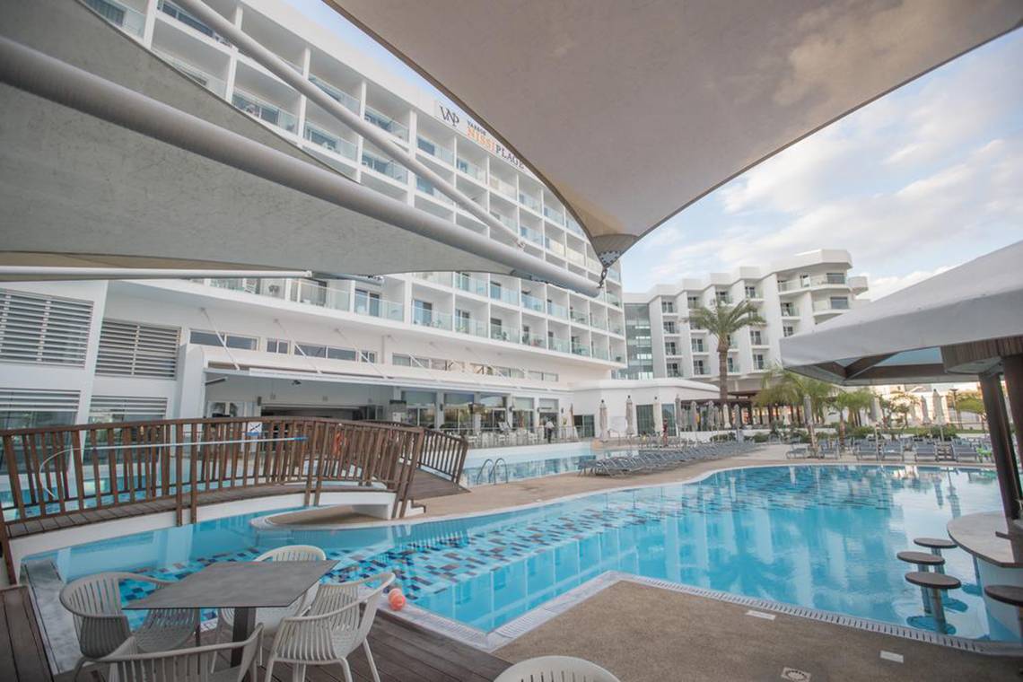 Poolbereich des Vassos Nissi Plage Hotels mit Liegestühlen und Gebäuden im Hintergrund.