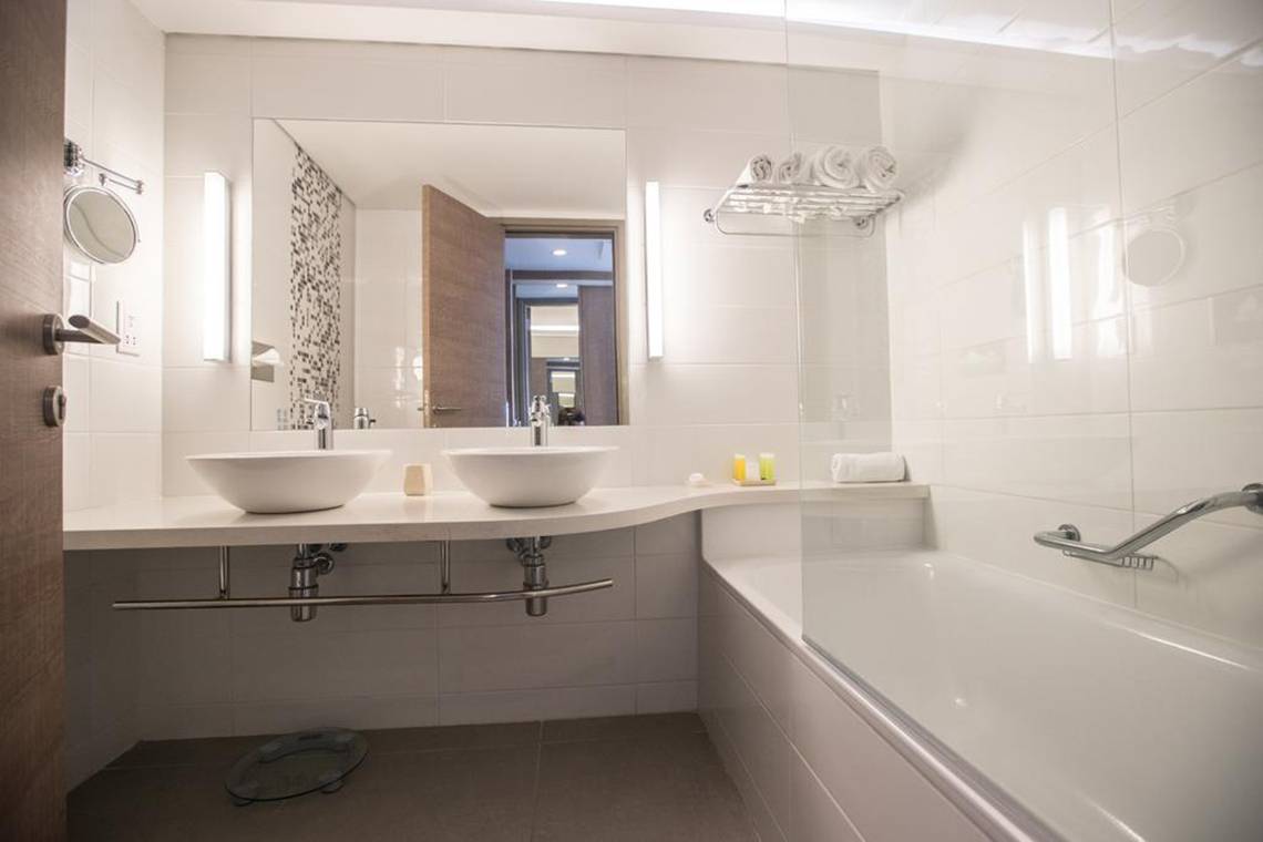 Badezimmer im Vassos Nissi Plage Hotel mit zwei Waschbecken, einem Spiegel und einer Badewanne.