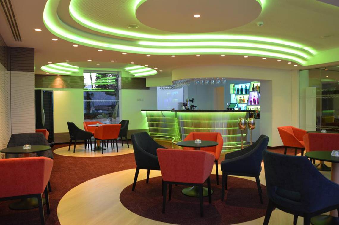 Loungebereich des Vassos Nissi Plage Hotels mit grünen Lichtern an der Decke und modernen Möbeln.