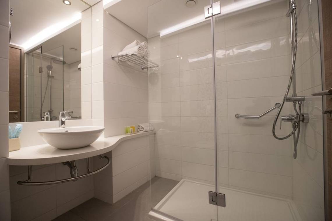 Ein modernes Badezimmer im Vassos Nissi Plage Hotel mit einer Dusche, Waschbecken und Handtüchern.