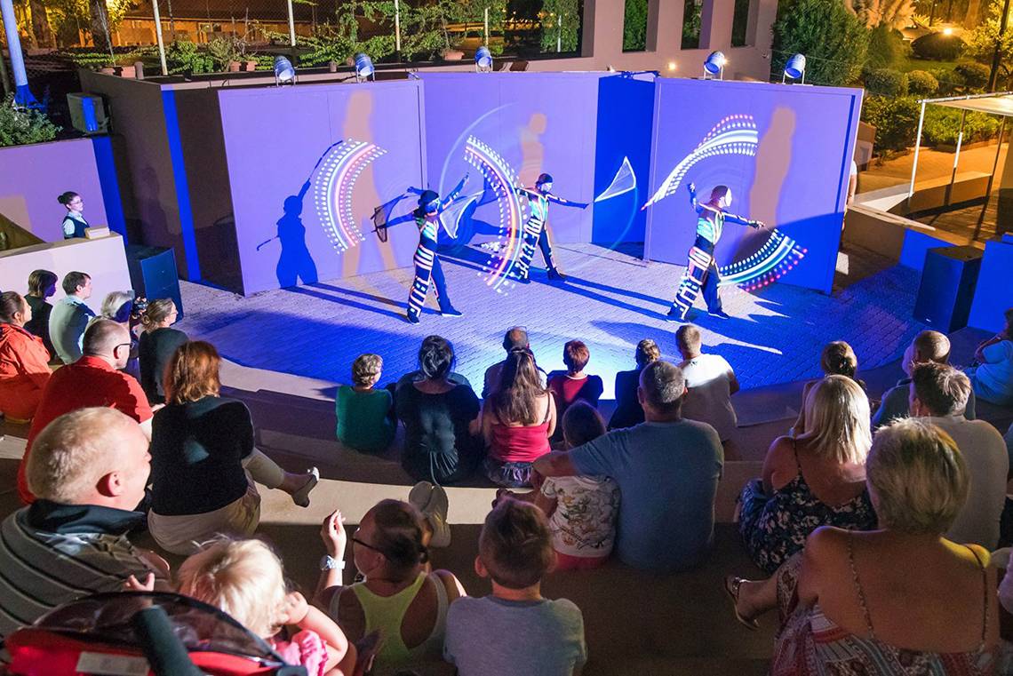 Besucher des Blue Bay Resorts beobachten eine Aufführung mit Lichteffekten auf der Bühne.