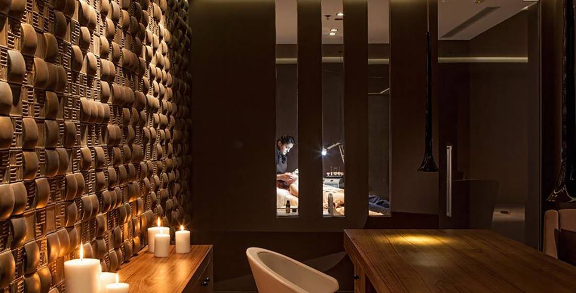 Behandlungsraum im Aqua Blu Boutique Hotel & Spa mit gemusterter Wand, drei brennenden Kerzen und einem Mann, der eine Massage durchführt.