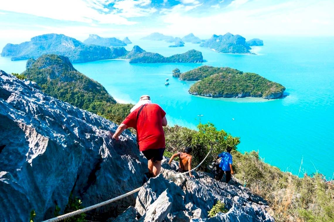 Personen steigen auf Felsen mit Aussicht auf Meer und Inseln