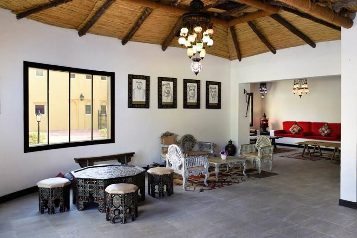 Loungebereich im Al Hamra Village mit Möbeln, Lampen und Porträts an der Wand.
