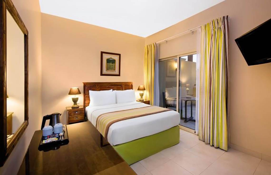 Doppelbettzimmer im Al Hamra Village Hotel mit Balkon und Fernseher.