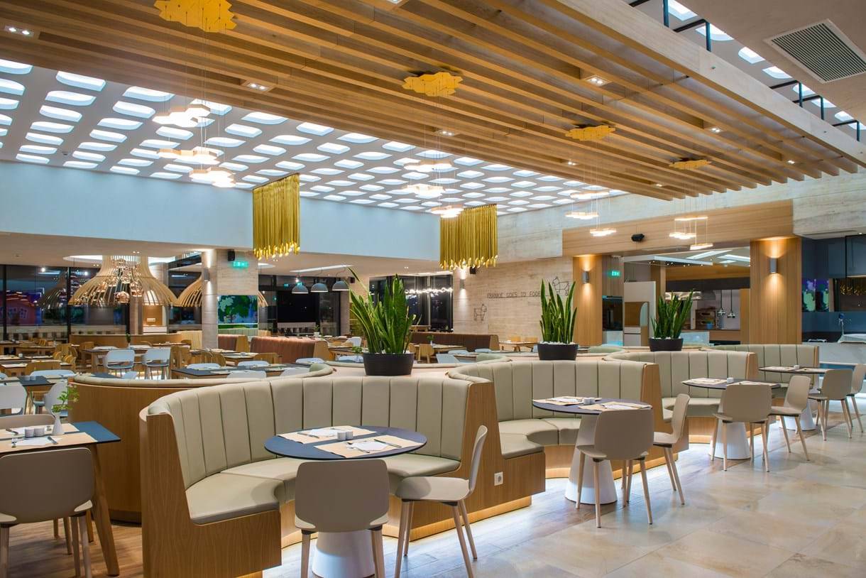 Innenansicht des Restaurants im Fodele Beach & Water Park Holiday Resort mit Holzmöbeln und Pflanzen.