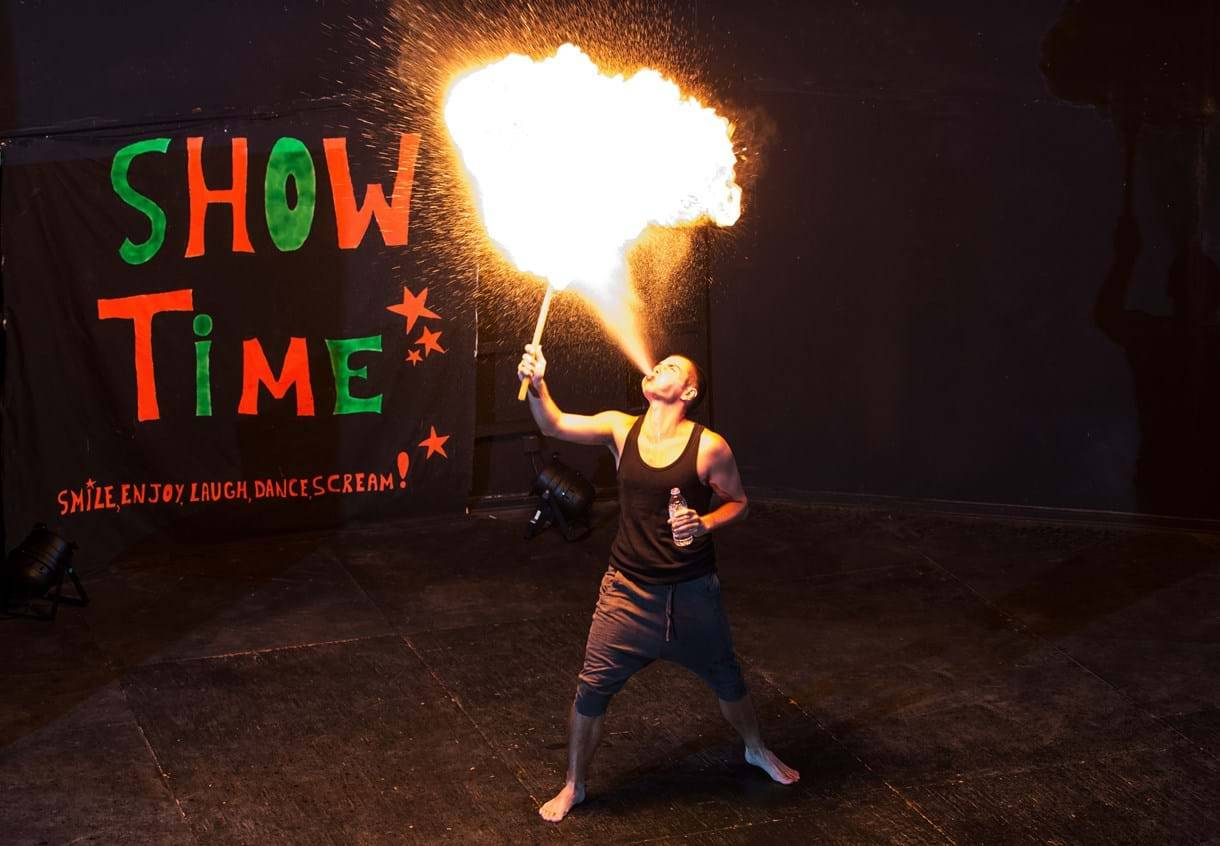 Mann blaest Feuer aus seinem Mund auf einer Show-Buehne.
