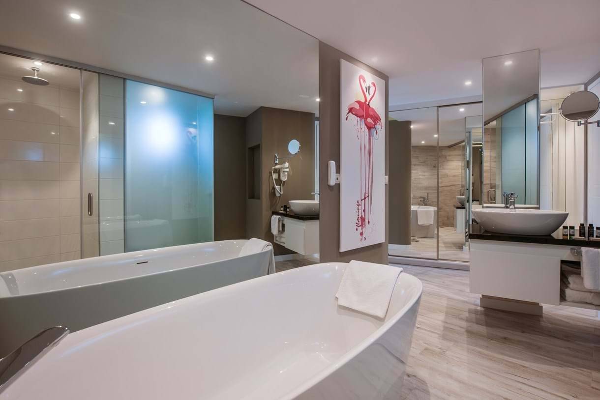 Modernes Badezimmer mit zwei Badewannen, Waschbecken, und Flamingo-Wandbild im Fodele Beach & Water Park Holiday Resort.