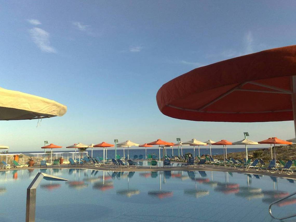 Außenpool des Aktea Beach Village Hotels mit Sonnenschirmen und Liegestühlen am Meer