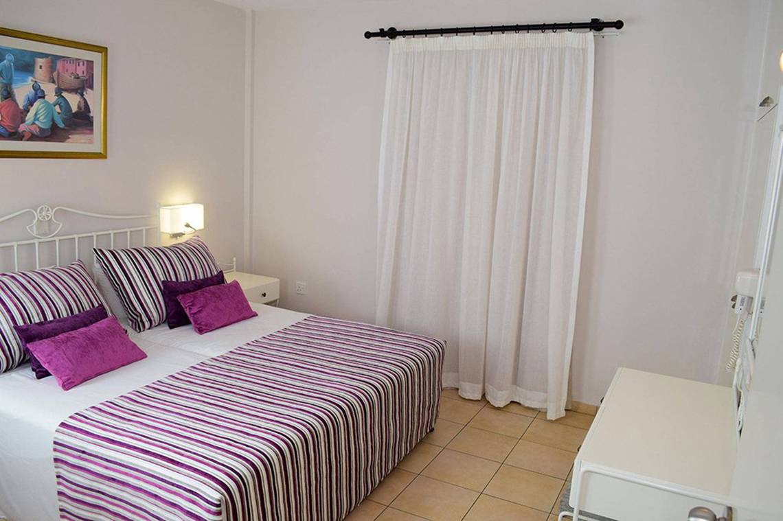 Ein modernes Schlafzimmer im Aktea Beach Village Hotel mit einem Doppelbett, farbigen Kissen und weißen Vorhängen.