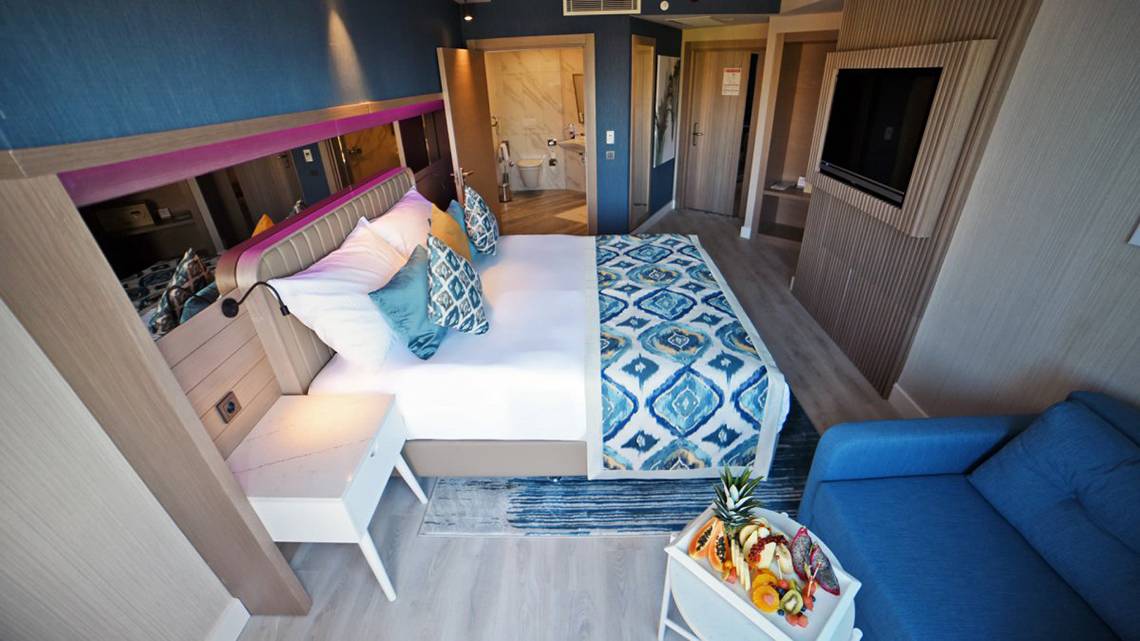 Innenansicht der Suite im Royal Wings Hotel mit Bett, Couch, Nachttischen und Fernseher.