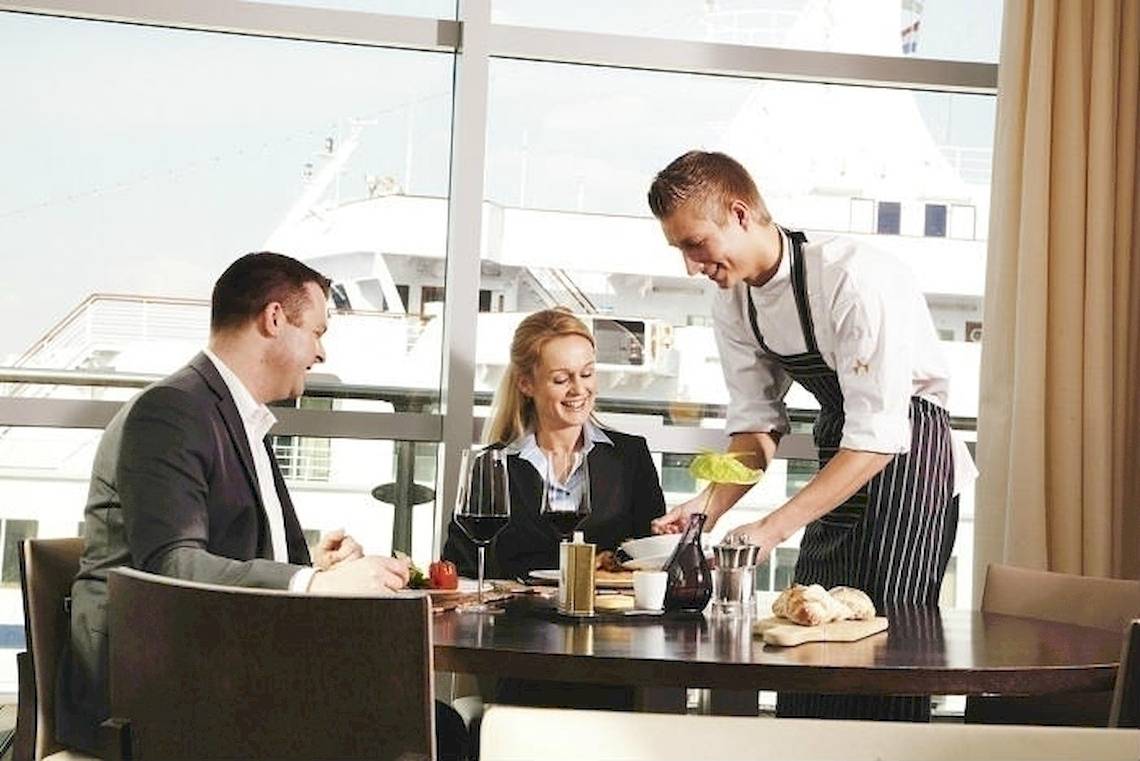 Ein Kellner serviert ein Essen in einem Restaurant mit Blick auf ein Schiff.
