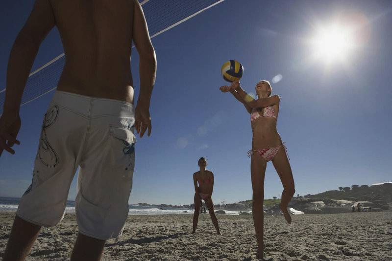 Volleyball-Spieler auf dem Strand mit der Sonne im Hintergrund.