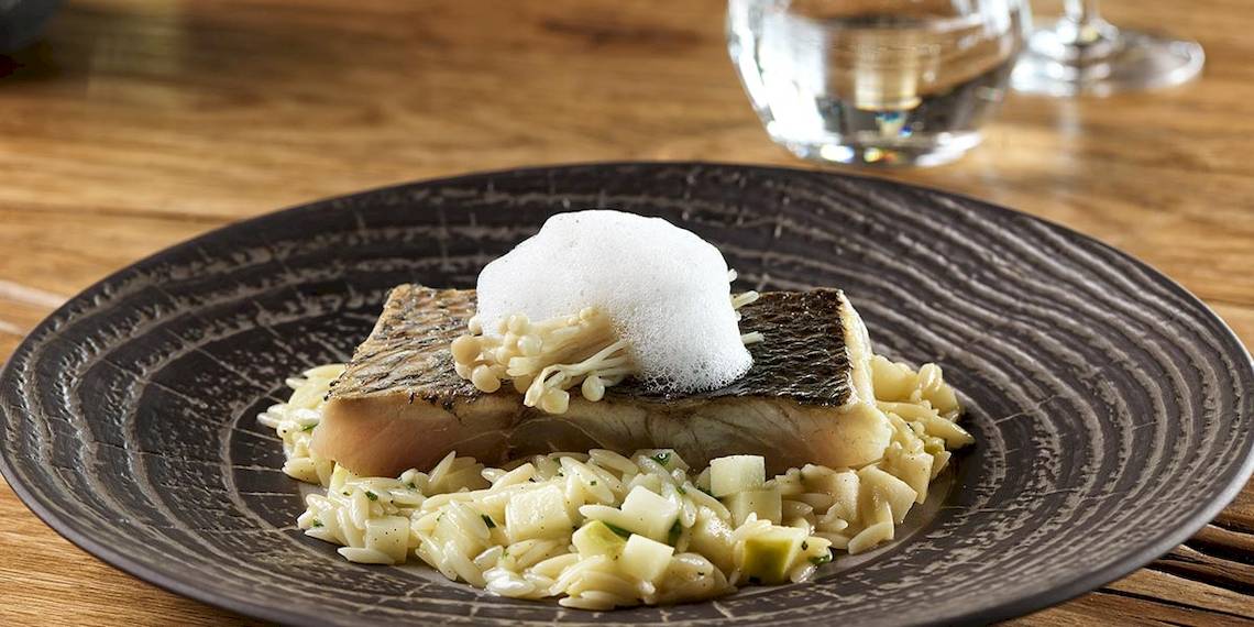 Fischgericht mit Reis und Gemüse auf einem schwarzen Teller auf einem Holztisch.