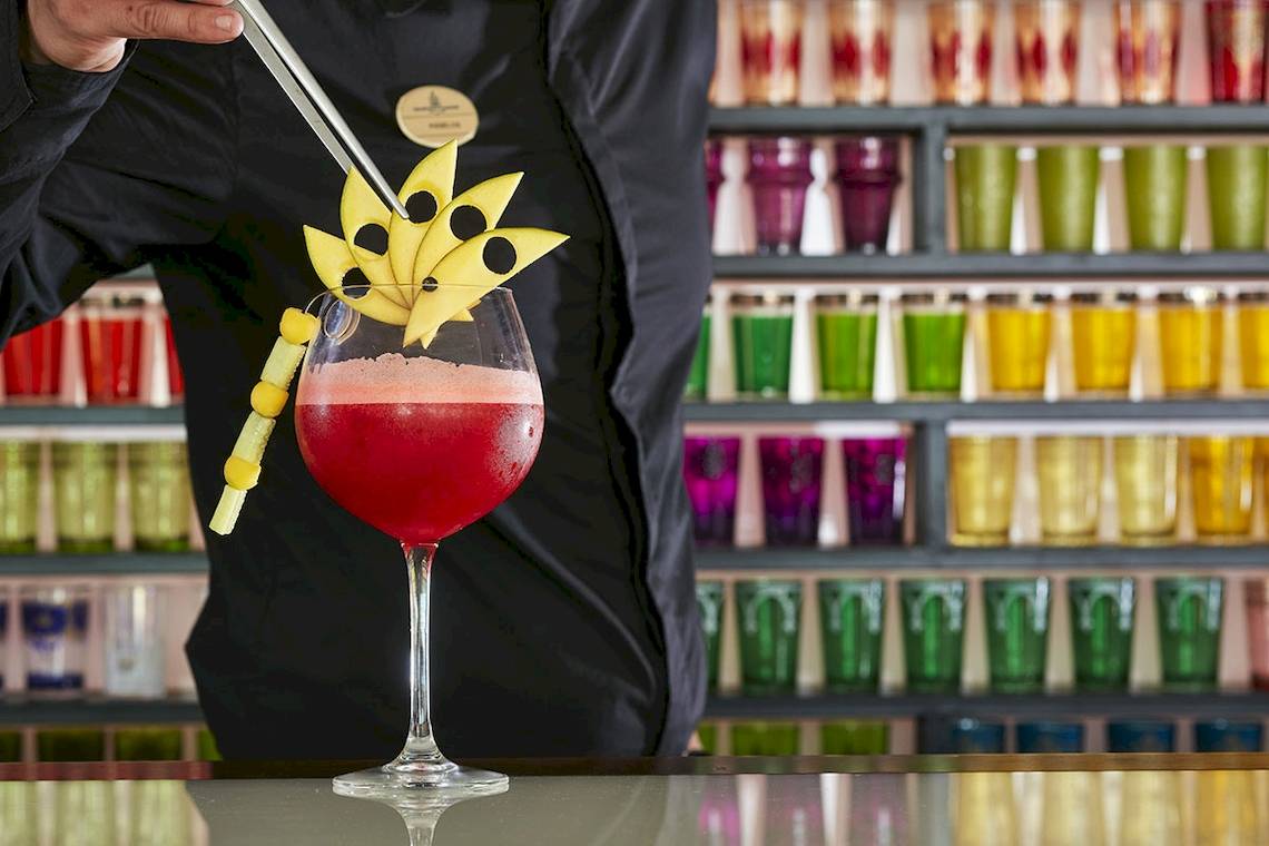 Ein Barkeeper im Myconian Imperial bereitet einen Cocktail in einem Glas zu, der mit einer gelben Blume garniert ist.