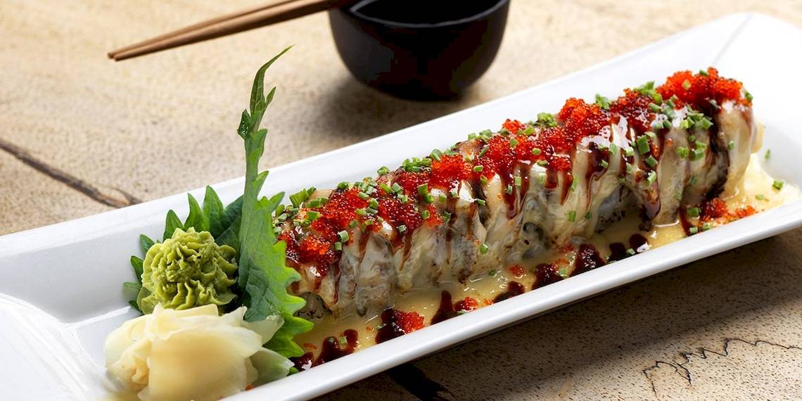 Eine Sushi-Rolle mit roter Kaviar- und Sojasaucen-Belag auf einem weißen Teller.
