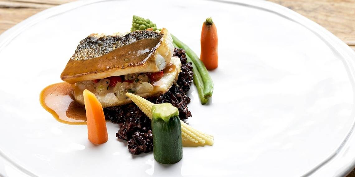 Ein Fischgericht auf einem weißen Teller, umgeben von gebratenem Reis und Gemüse.