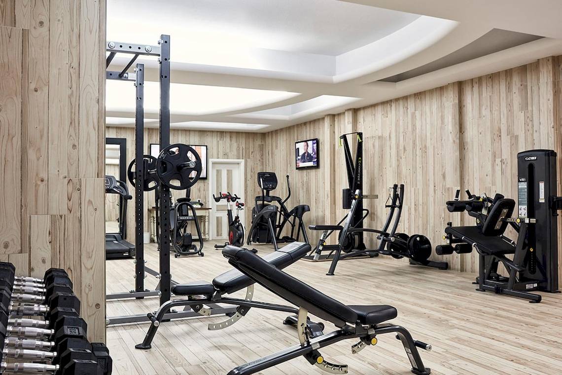 Fitnessraum im Myconian Imperial Hotel mit Holzboden und verschiedenen Trainingsgeräten.