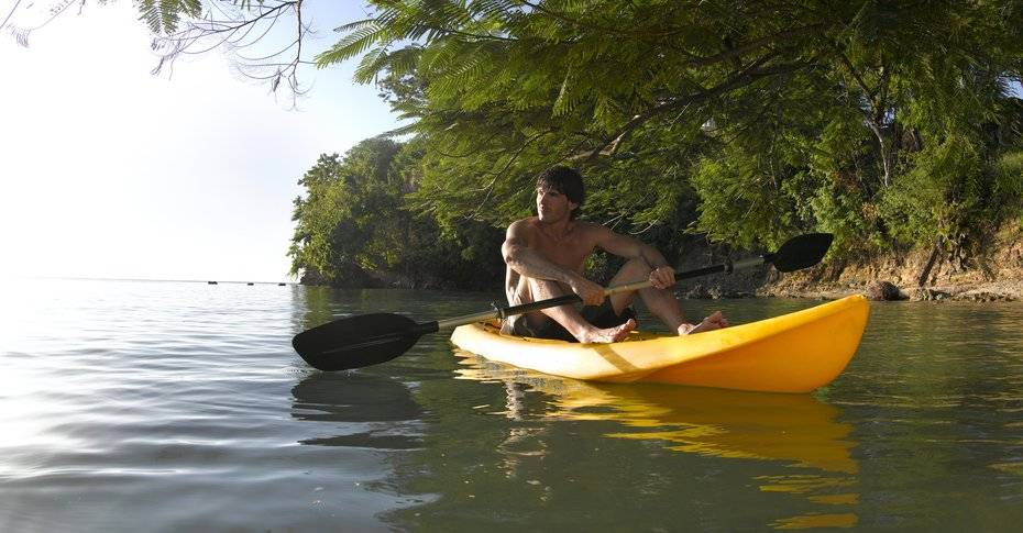 Ein Mann ohne Oberteil paddelt in einem gelben Kajak auf dem Wasser.