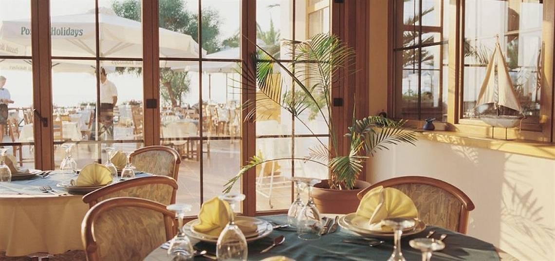 Innenansicht des Restaurants im Possidi Holidays Resort & Suites mit gedeckten Tischen und großen Fenstern.