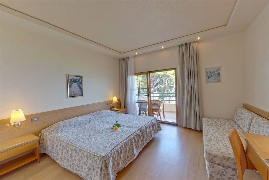 Schlafzimmer im Possidi Holidays Resort & Suites mit Doppelbett, Sofa und Balkon.