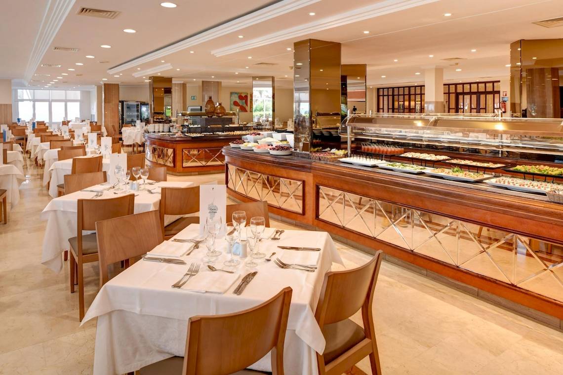 Innenansicht des Restaurants des Hipotels Flamenco Hotel mit vielen Tischen und Stühlen, einer langen Theke und verschiedenen Speisen.