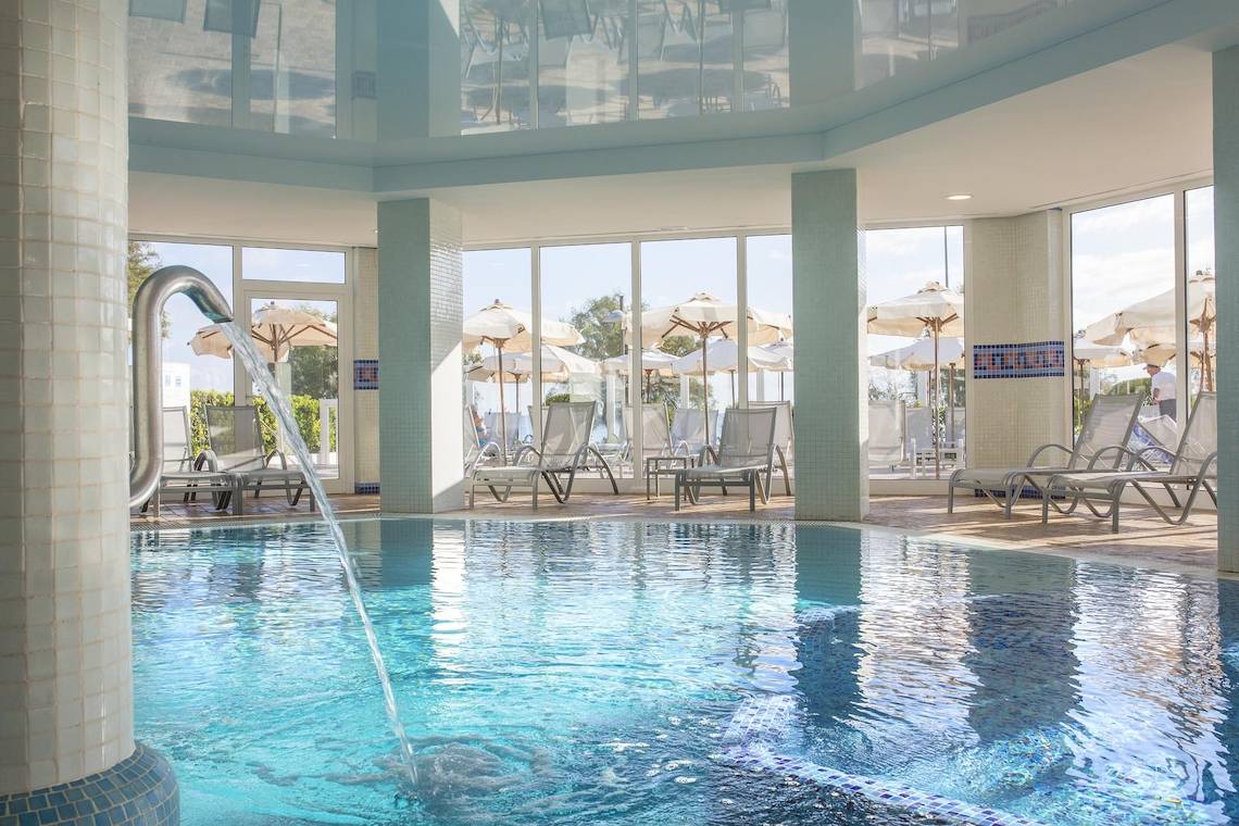 Pool im Hipotels Flamenco Hotel mit Loungestühlen und Sonnenschirmen.
