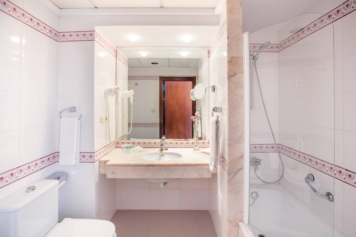 Badezimmer des Hipotels Flamenco mit Waschbecken, Spiegel und Dusche.