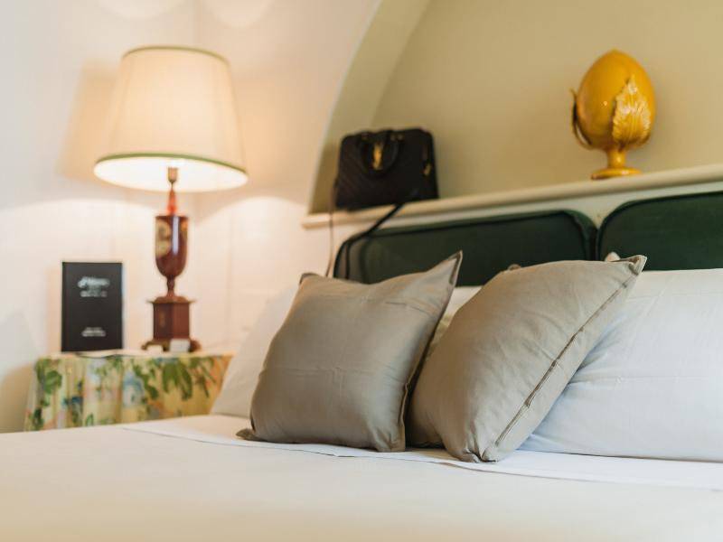 Doppelbett mit zwei Kissen, Lampen und Taschen im Zimmer im Hotel Il Melograno