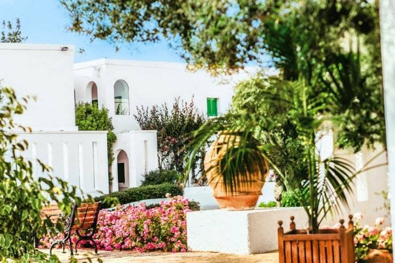 Außenbereich des Il Melograno Hotels mit weißen Gebäuden, Blumen und Pflanzen.