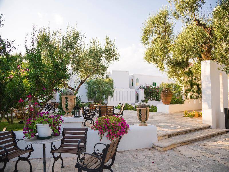 Gartenbereich des Il Melograno Hotels mit Bäumen, Bänken und Tischen.