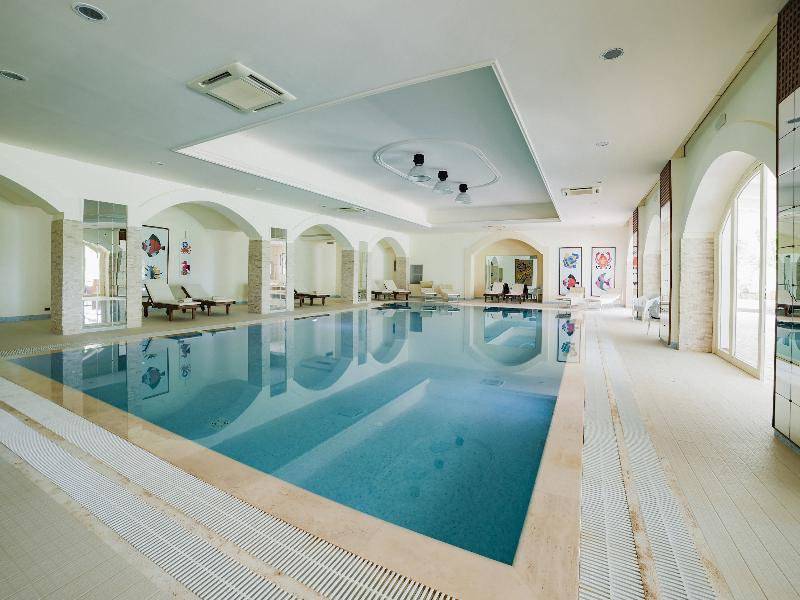 Innenpool des Hotels Il Melograno mit weißen Fliesen und Lounge-Bereichen.