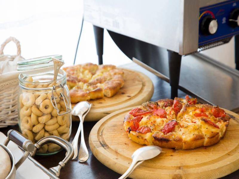 Tisch mit zwei Pizzen, einer Glasflasche mit Gebaecken und verschiedenen Essgeschirr auf dem Tisch